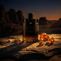 Azzaro perfume bottle on rocky surface with amber stones and cardamom pods at sunset