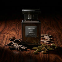 Tom Ford Oud Wood perfume bottle with oud chips and cardamom pods on wooden surface