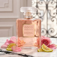 Coco Mademoiselle Chanel perfume bottle with pink rose petals and citrus slices on marble
