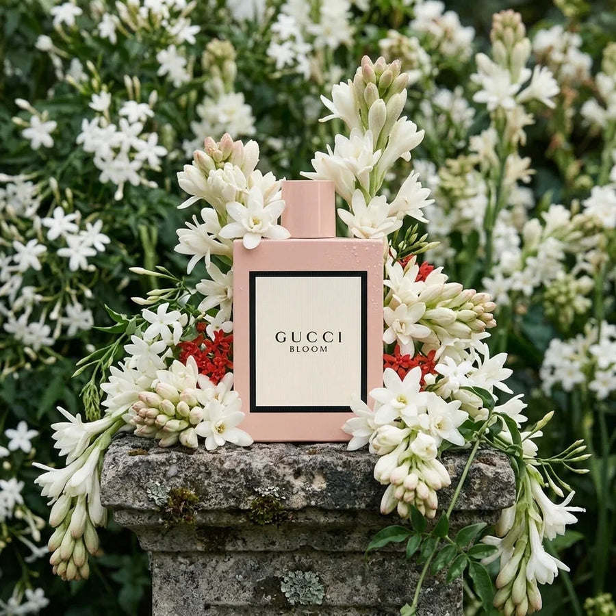 Gucci Bloom perfume bottle surrounded by white flowers on a stone pedestal outdoors