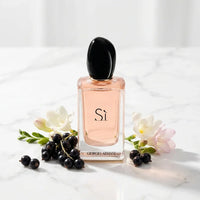 Giorgio Armani Si perfume bottle with blackcurrants and white flowers on marble surface