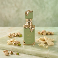 Green and gold Eclaire Pistache perfume bottle with pistachios and white chocolate on marble