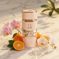 Yara perfume bottle with gold accents, surrounded by orchids and fresh oranges on marble.